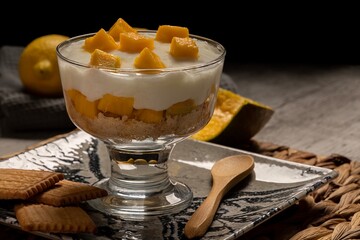 Delicious glass of cold yogurt mousse with mango and biscuit, dark food style.
