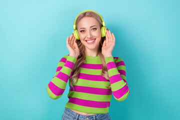Portrait of optimistic girl with wavy hairdo wear stylish clothes touching headphones listen playlist isolated on blue color background