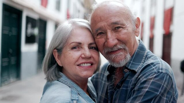Happy multiracial senior couple hugging each other with city on background - Elderly people relationship family concept