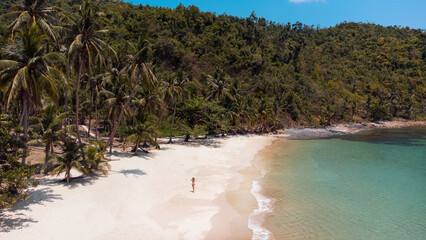Piękna rajska plaża z białym piaskiem, palmami i turkusową wodą, osoba idąca po wybrzeżu. - obrazy, fototapety, plakaty