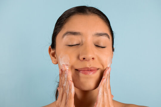 Ethnic woman applying soap on cheeks during beauty procedure