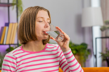 Thirsty brunette woman holding glass of natural aqua make sips drinking still water preventing dehydration sits at home living room. Girl with good life habits, healthy slimming, weight loss concept