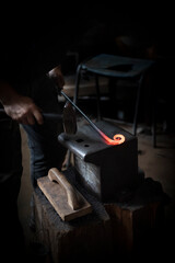 Fototapeta na wymiar Man in a dark forge workshop forging red hot steel with a hammer on an iron anvil