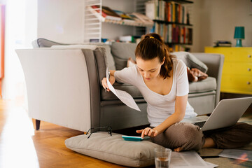 Young woman going over her bills at home while working on the laptop in the living room