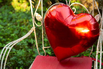 close de um Balão de coração metalizado recostado em uma cadeira de ferro branca de estilo...