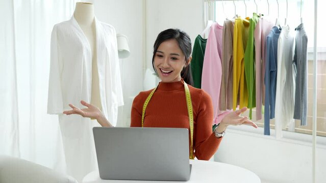 Woman designer entrepreneur showing clothes product on live online social media streaming and packing into cardboard box to preparing for shipping customer delivery at home