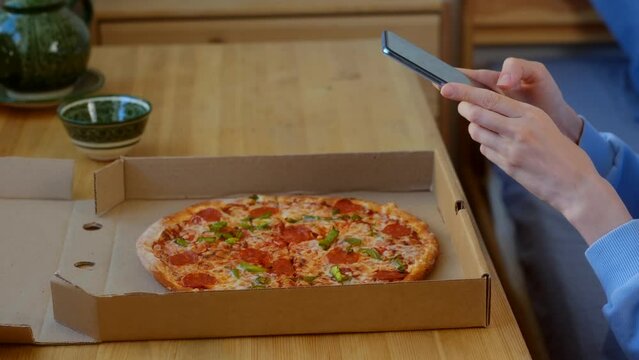 Blogger take a picture fresh pizza with sausage. view side - Photograph hands use smartphone photographing appetizing fresh cooked italian Pizza on wooden table. Food blog of blogging. Technology