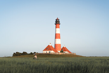 Fototapeta na wymiar girl with a bicycle on the background of Westerheversand Lighthouse in Germany