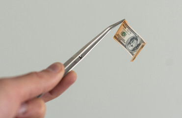 Lab, forensic scientist or medical professional with tweezers takes out rolled-up money. Hands in white gloves hold a test tube with a hundred dollar bill.