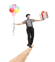 Cheerful mime walking on a wooden beam and carrying balloons and a gift box