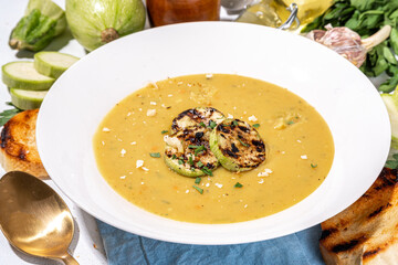 Squash vegetable marrow cream soup, white zucchini pureed soup with grilled marrow or zucchini slices, cheese and greens, white concrete table background copy space