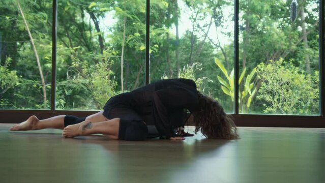 Female dancer moves in energetic and sensual ways at dancehall workout. Young caucasian woman moves her body smoothly lying on floor in dance studio, green forest in background, zoom in shot