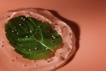 A drop of cosmetic gel with mint leaf on a pink background.