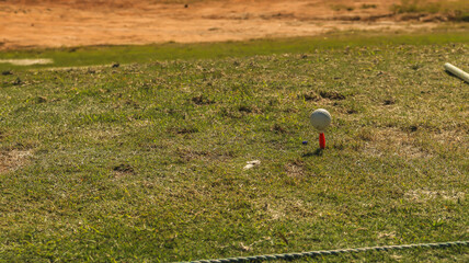 Bola de golfe em cima de um tee em um gramado falhado de um campo de golfe
