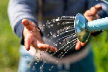 A toddler washes his hands in the garden with a watering can