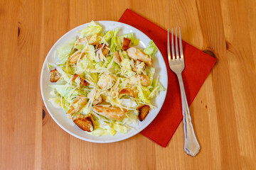 Fresh healthy caesar salad with chicken breast, lettuce, parmesan cheese, dressing and croutons on wooden table. Top view