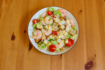 Fresh healthy caesar salad with prawns, cherry tomatoes, lettuce, parmesan cheese, dressing and croutons on wooden table. Top view