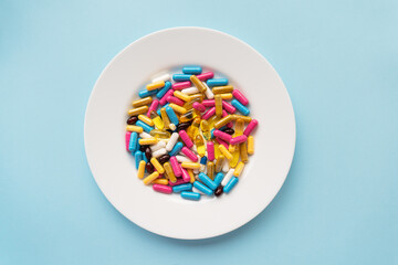 Colorful pills in a large white bowl on a blue background. The concept of health and evidence-based...