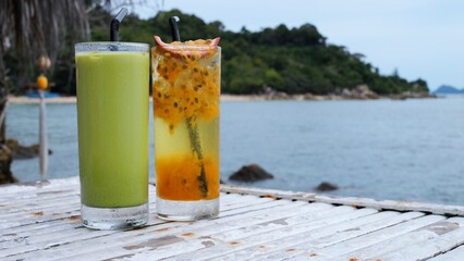 A hand puts a wooden tray with pizza on the table. Green smoothie with ice cubes and a drink with a slice of passion fruit. Healthy pizza lunch with tomatoes. Concept eating healthy pizza by the ocean