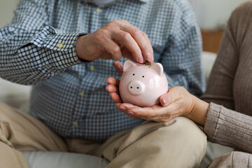 Saving money investment for future. Senior adult mature couple hands putting money coin in piggy...