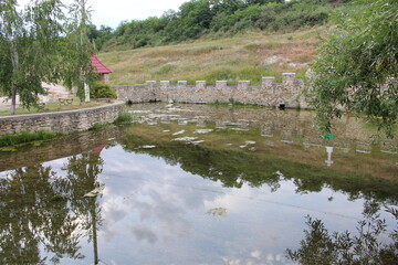Fototapeta na wymiar A pond with a stone wall and a building