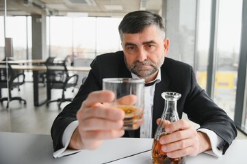 Old male employee drinking alcohol at workplace