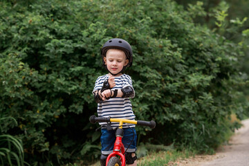 A cheerful little boy rides a running bike in a helmet outdoors. A happy child is engaged in an active sport. Protection. Life insurance and child safety.