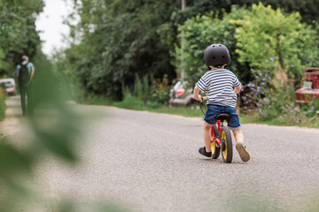 A cheerful little boy rides a running bike in a helmet outdoors. A happy child is engaged in an active sport. Protection. Life insurance and child safety.