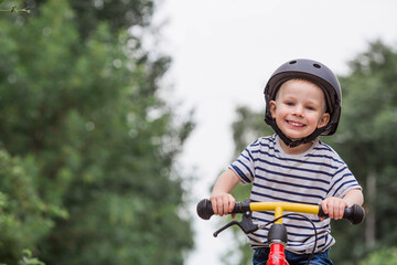 A cheerful little boy rides a running bike in a helmet outdoors. A happy child is engaged in an active sport. Protection. Life insurance and child safety.