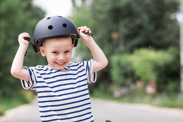 A cheerful little boy rides a running bike in a helmet outdoors. A happy child is engaged in an...