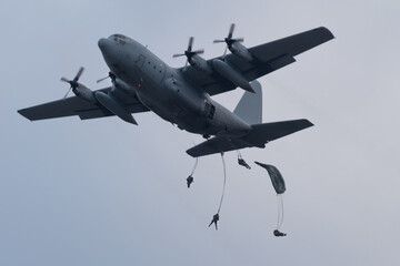 military logistic transport plane dropping paratroopers on a cloudy day at dawn