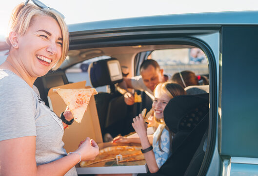 Positive smiling woman with slice of just cooked Italian pizza while family car trip stop. Happy family moments, childhood, fast food eating, family values or auto journey lunch break concept image.