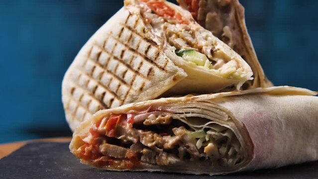 Close-up of a shawarma cut into three pieces on a black stone board. A delicious Arabic doner kebab. Traditional Turkish food. Greek gyros. Camera pans around. Parallax effect