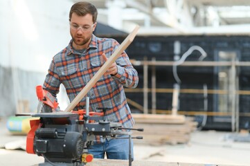 Professional carpenter using sawing machine for cutting wooden board at sawmill. Skilled cabinet...