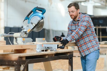Skilled cabinet maker cutting wood board with electric circular saw at woodworking sawmill....