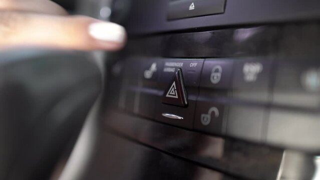 Close-up of woman fingers pressing emergency button on car dashboard, has problem