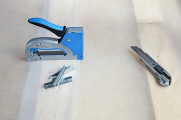 construction stapler, sharp knife and staples are on surface of material