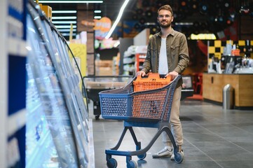 Handsome smiling man shopping in supermarket pushing trolley