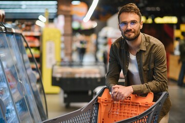 Handsome smiling man shopping in supermarket pushing trolley