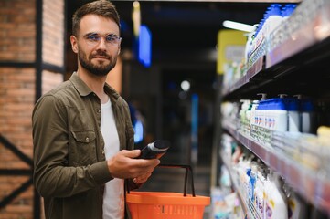 Smiling man chooses shampoo in supermarket