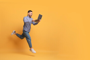 Fototapeta na wymiar Online Sales. Excited Asian Man With Laptop Computer Running Over Yellow Background