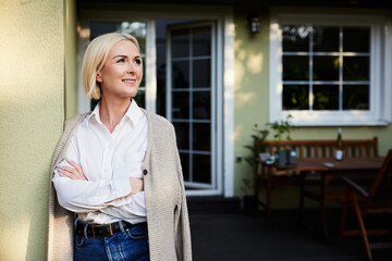 Home ownership. Portrait of mature woman standing on patio outside her house