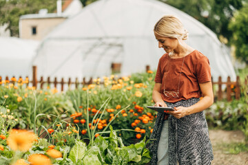 Young woman uses digital tablet for monitoring her garden.