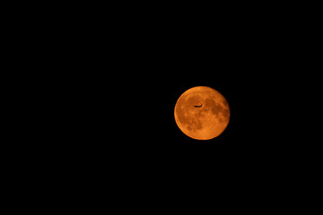 The full moon is red with an airplane flying in front of it. Supermoon.