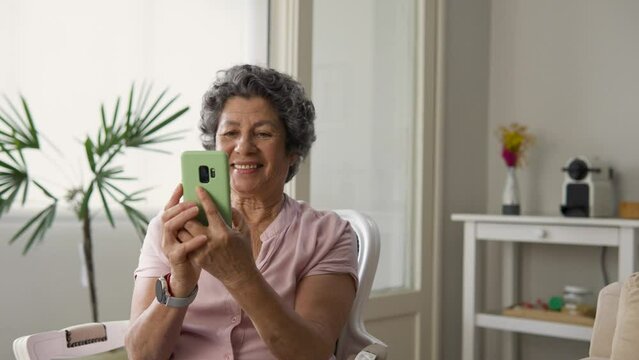 Watching video on mobile. excited Old aged short hair woman with smart phone enjoying online app and sitting in living room. 