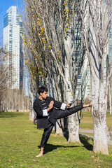 An athletic martial arts fighter practicing kicks in a public park. Copy space