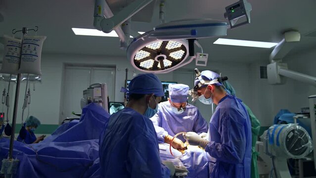 Innovatively equipped surgery room with a group of professional surgeons working in. Two neurosurgeons collaborate at operational table assisted by medical staff.