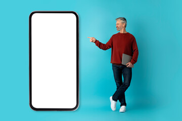 Middle aged man entrepreneur pointing at huge phone with mockup