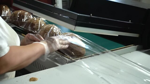 A female bakery worker packs sliced ​​bread using a specialized packaging machine. Packaging of bakery products before sending to the store shelves.