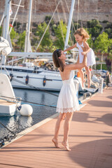 Happy mother and daughter child having fun on luxury yachts on background in marina. Family travel, lifestyle, vacation concept